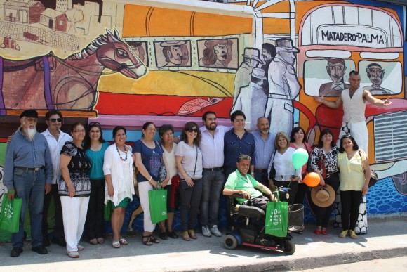 Vecinos que participaron del programa "Quiero mi Barrio" posan en frente al mural "Medios de Transporte".