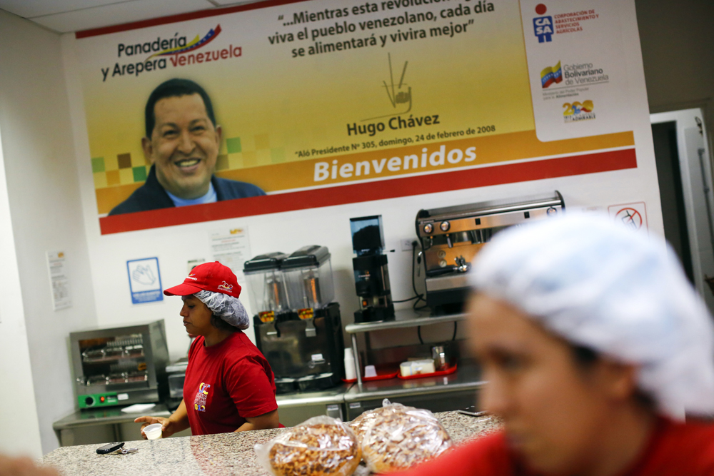 Women works at a bakery with a poster of late president Hugo Chavez in Ciudad Caribia