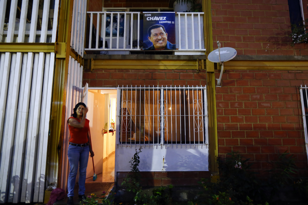 A woman stands outside her apartment next to a portrait of the late Venezuelan President Hugo Chavez in Ciudad Caribia outside Caracas