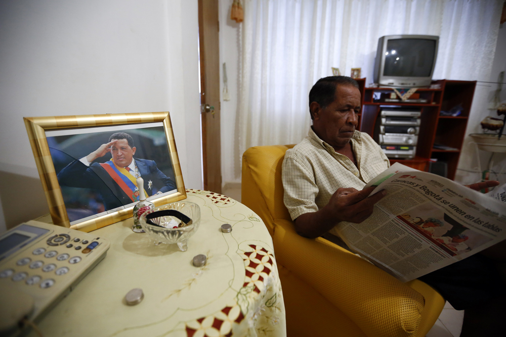 A man reads a newspaper at his apartment next to a portrait of the late Venezuelan President Hugo Chavez in Ciudad Caribia outside Caracas